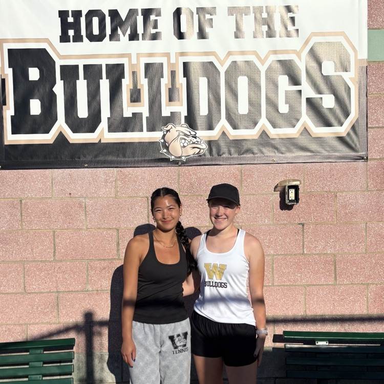 Two tennis players in front of a home of the Bulldogs sign
