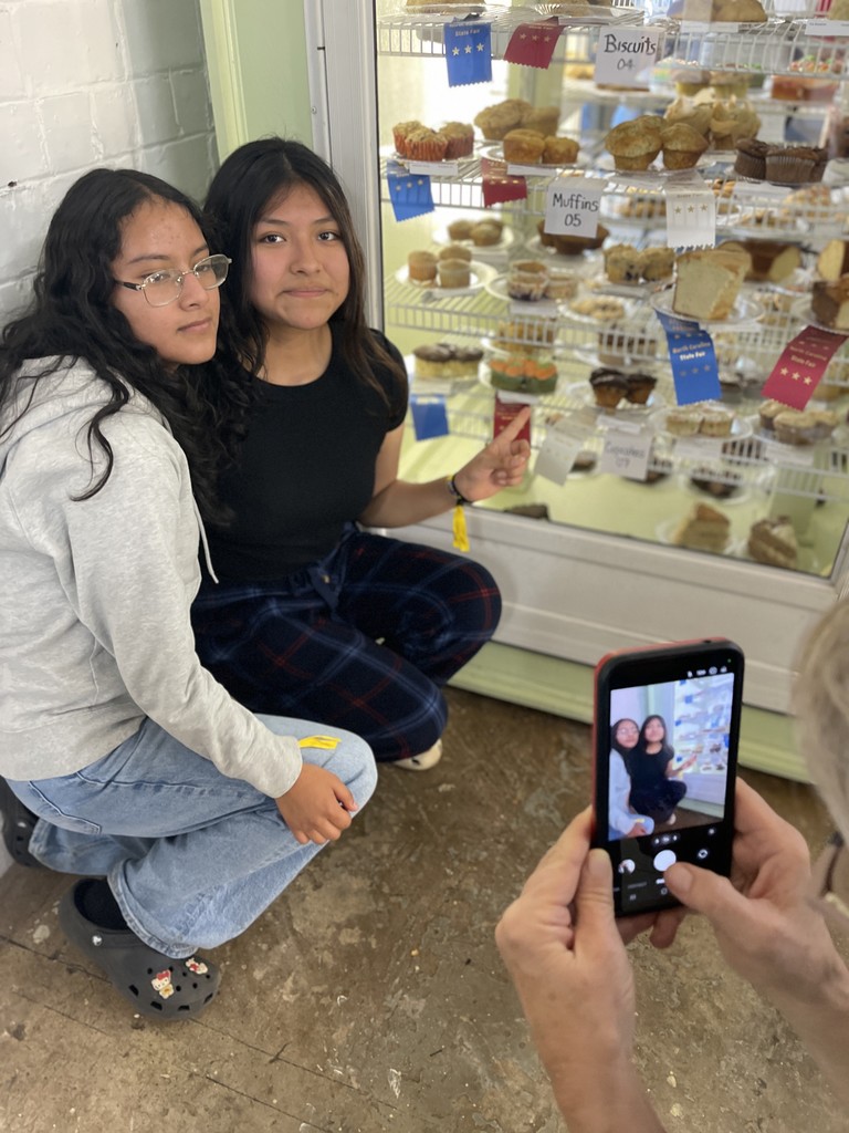 Two students pose for a photo in front of a glass display case full of baked goods