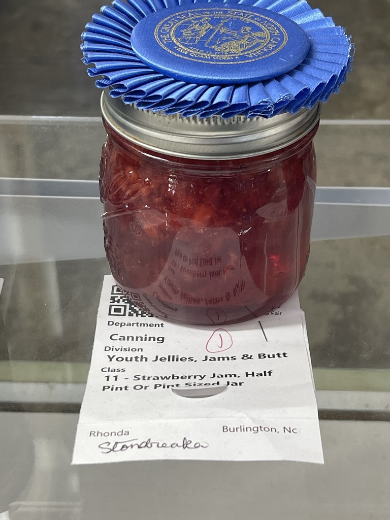 A jar of strawberry jam with a blue ribbon on top