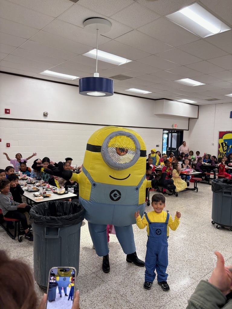 A large minion costumed person stands with a smaller child in a minion costume giving a thumbs up in the school cafeteria