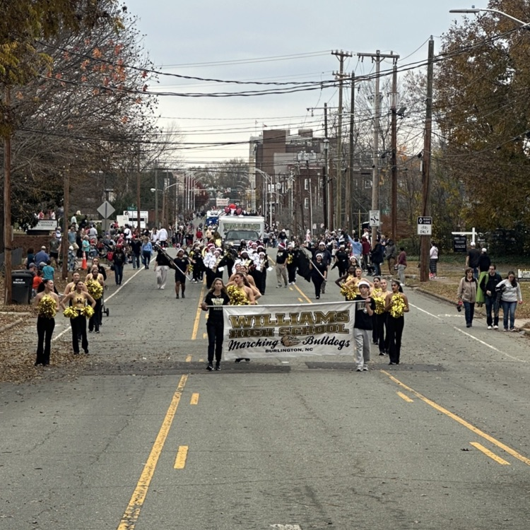 students holding WHS banner with dance team and band behind it on a street 