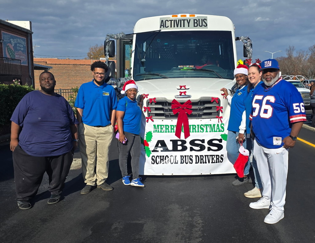 ABSS bus drivers standing in front of a white activity bus decorated for a Christmas parade