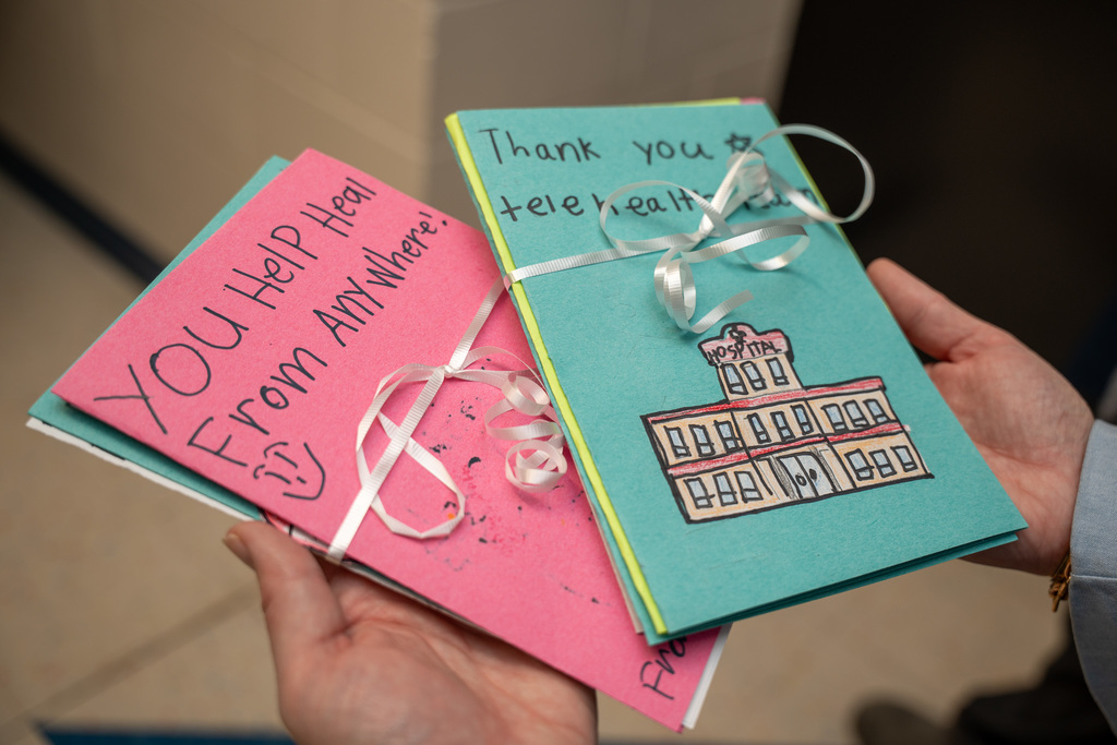 Close-up of two colorful, handmade cards tied with a ribbon. One card reads "YOU Help Heal From Anywhere!" and the other shows a drawing of a hospital and reads "Thank you to telehealth."