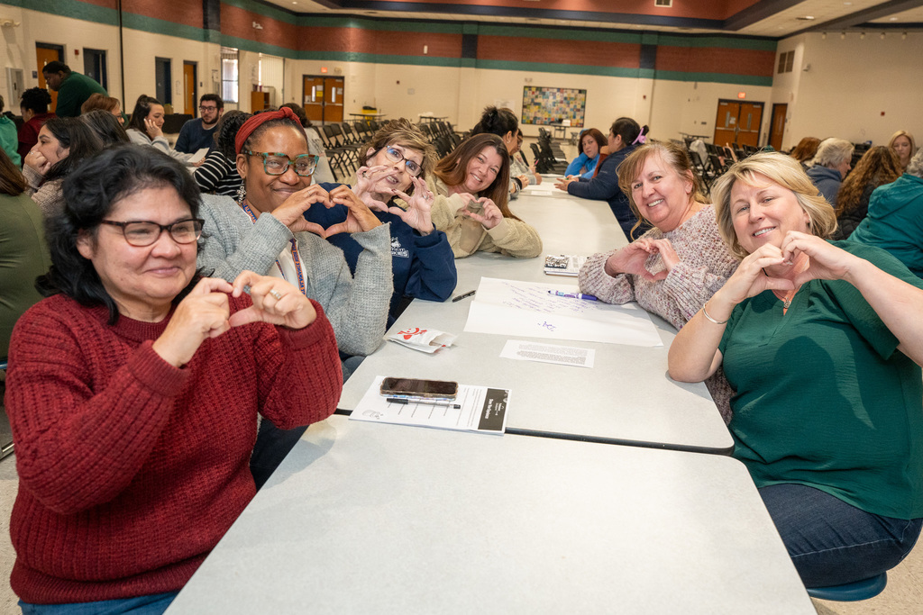 Multiple office staff from schools make a heart gesture with their hands