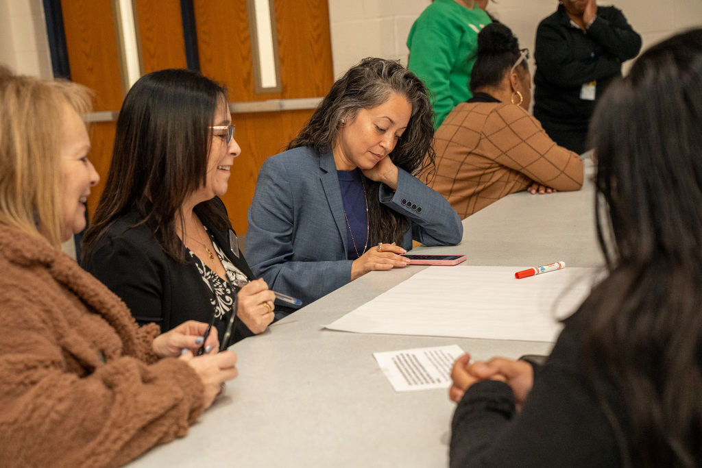 Multiple admin staff from central office look towards a phone and poster paper during a group exercise for a professional development session