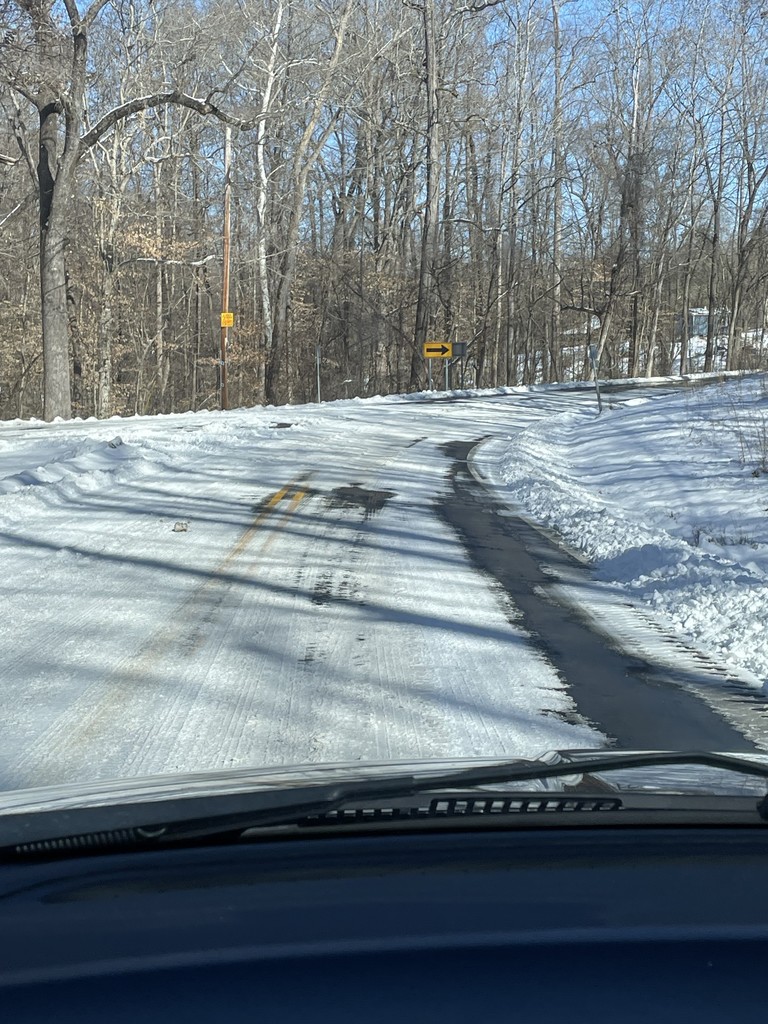 A snow and ice covered road with trees on either side.