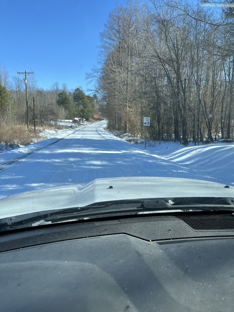 A snow and ice covered road with trees on either side.