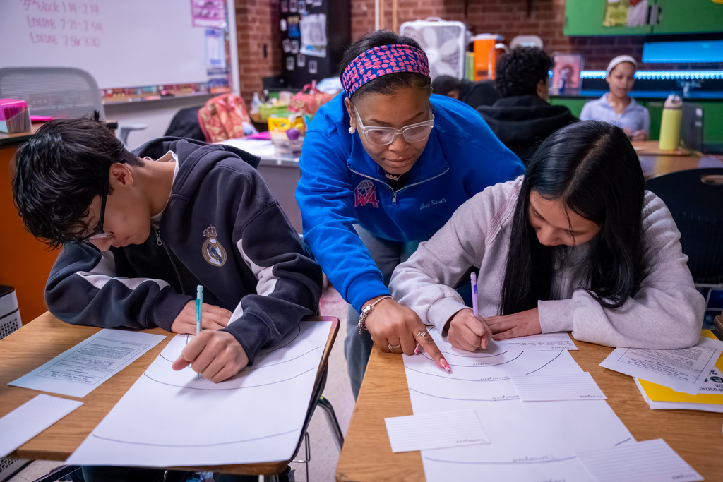 A teacher leans over and points to a term on a student-created diagram of atmospheric levels
