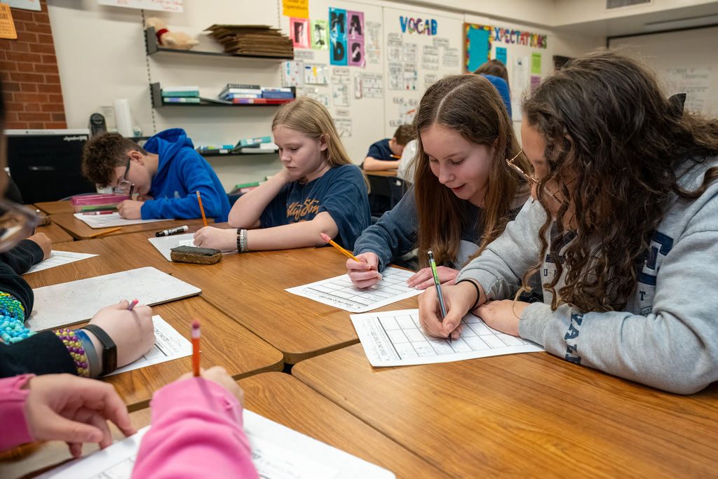Multiple middle school students at their desks which are clustered together, all working on two-step math problems
