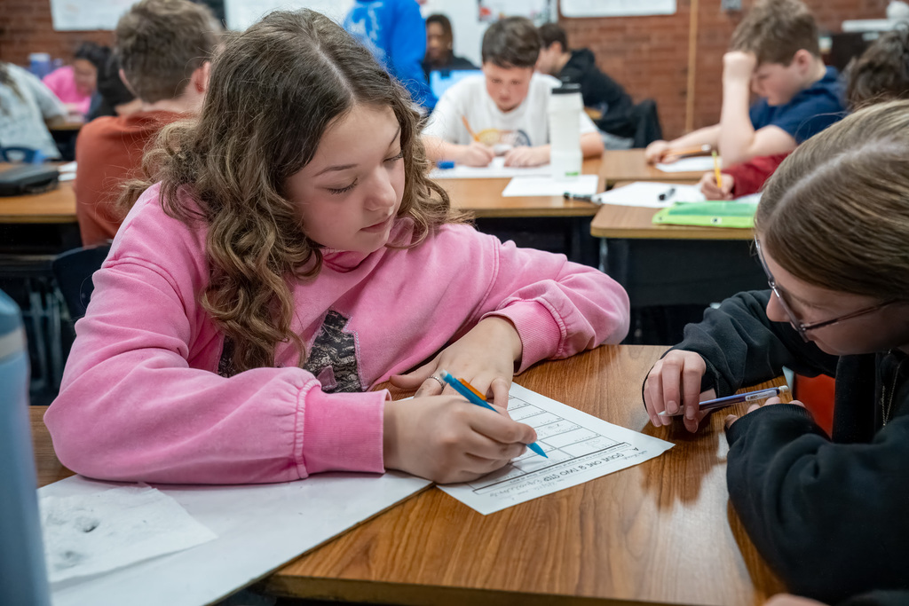 A student gestures towards a two-step math problem on her paper