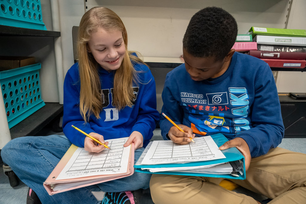 Two students sit beside each other on the floor while working on two-step math problems