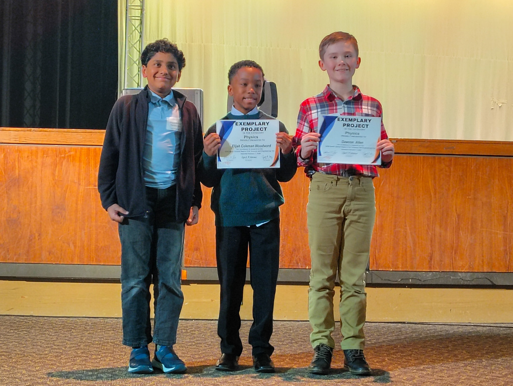 Three young participants in the Region 5 science fair on stage being recognized