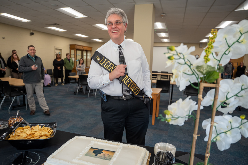 Dave speaking into a microphone in front of a cake