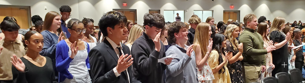 rows of smiling students raise their right hands and recite the NHS pledge during the induction ceremony