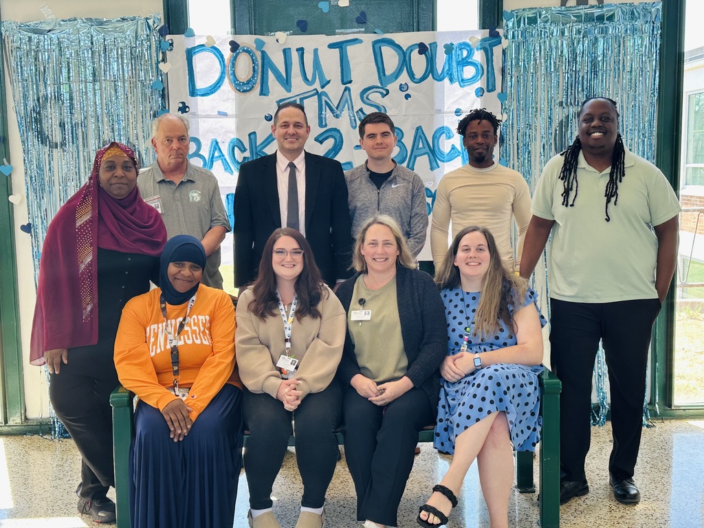A group of Turrentine Middle School staff posed in front of a Donut Doubt TMS backdrop with blue streamers