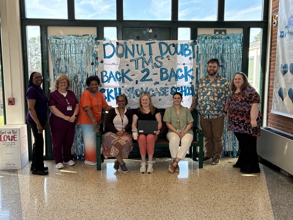 A group of Turrentine Middle School staff posed in front of a Donut Doubt TMS backdrop with blue streamers
