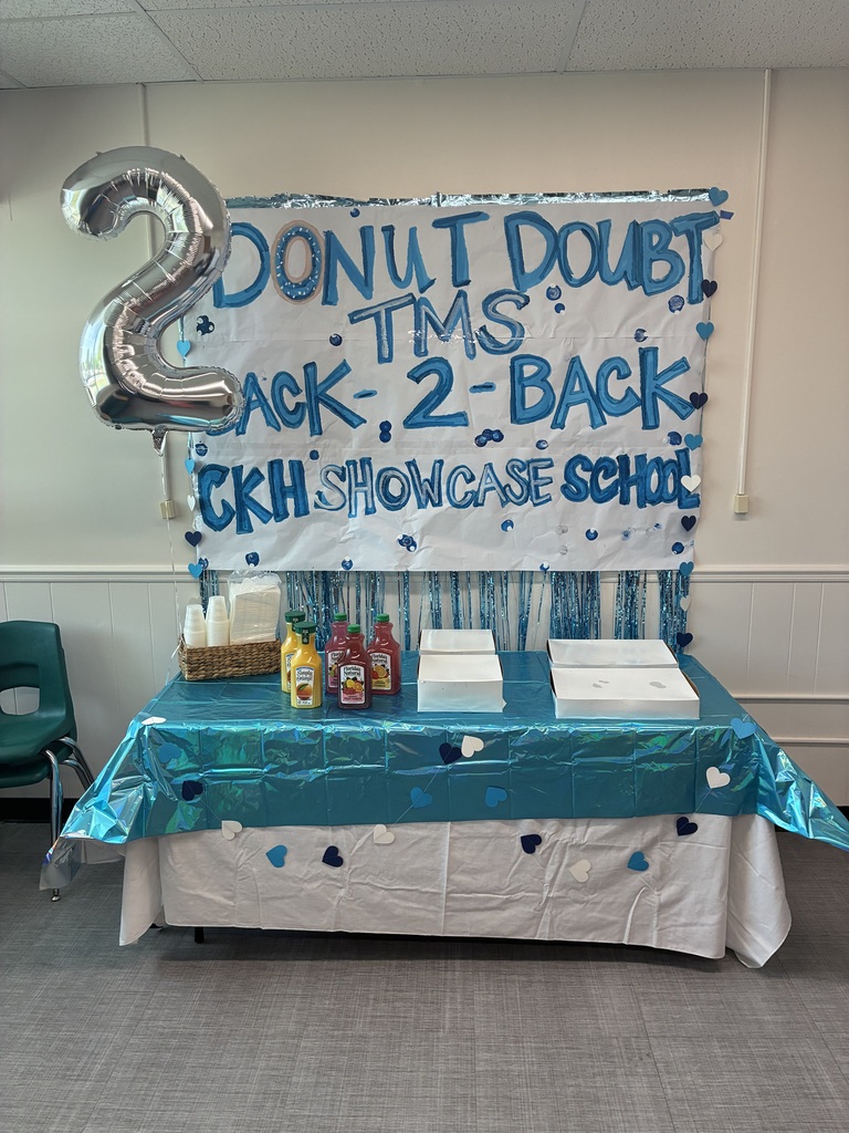 A table display celebrating TMS being a National Showcase School.  On the table are various juices and boxes of dougnuts.
