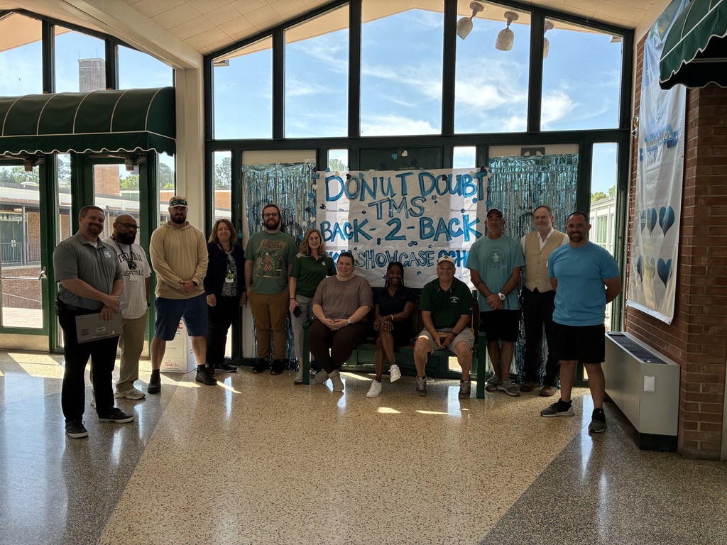 A group of Turrentine Middle School staff posed in front of a Donut Doubt TMS backdrop with blue streamers
