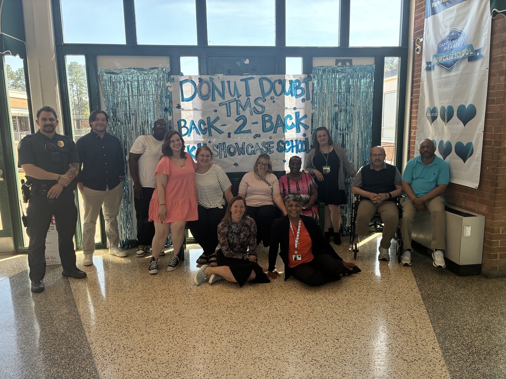 A group of Turrentine Middle School staff posed in front of a Donut Doubt TMS backdrop with blue streamers