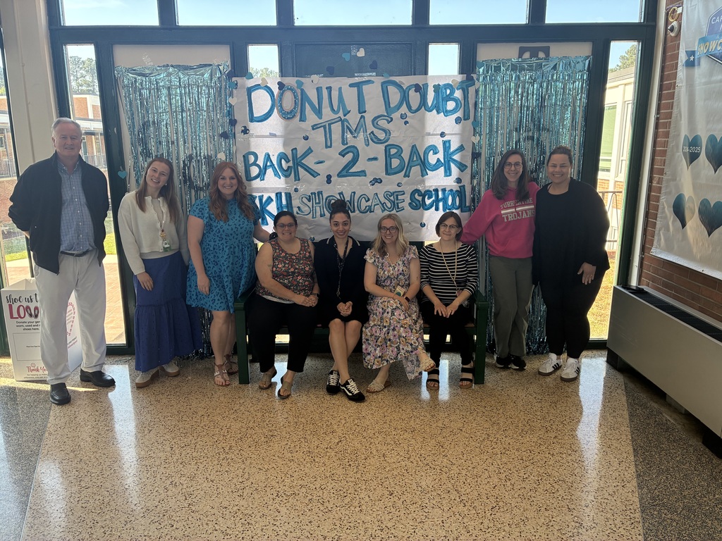 A group of Turrentine Middle School staff posed in front of a Donut Doubt TMS backdrop with blue streamers