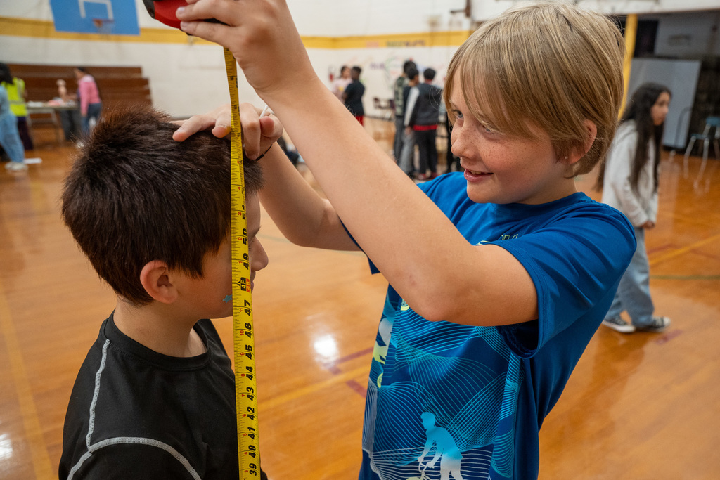 A young boy at Haw River Elementary smiles as he uses a yellow measuring tape to check the height of a classmate during a health and nursing career demonstration in the school gymnasium.