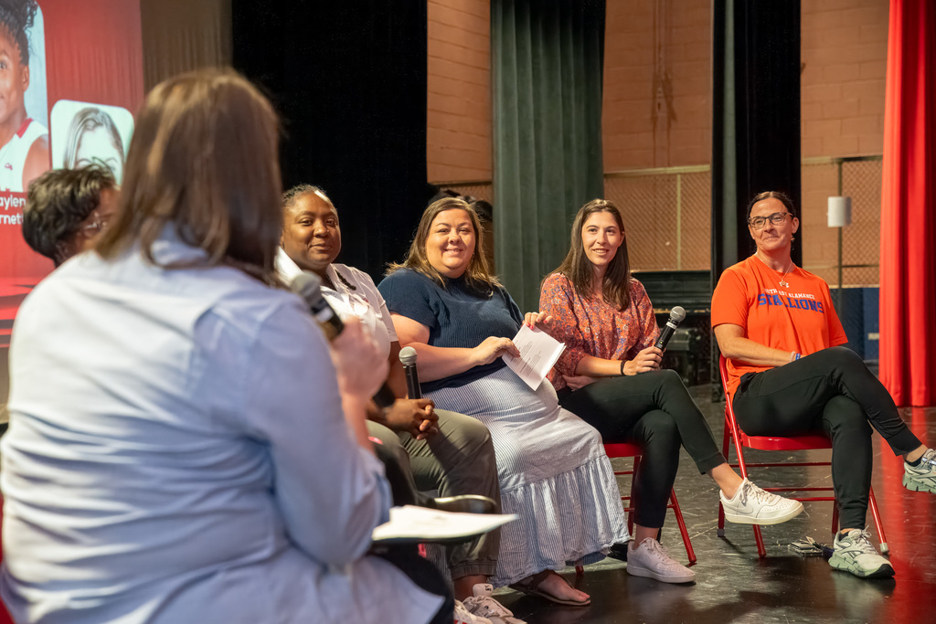 A close-up, angled shot from behind the moderator showing five members of the discussion panel—including Stephanie Smith and Tameka Harvey—as they engage in conversation during the event.