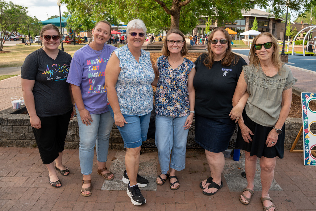 A group of six women, including staff from various ABSS elementary schools, pose together on a paved walkway at Burlington Carousel Park.