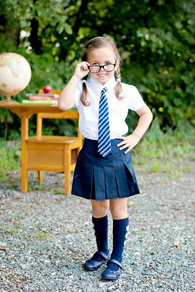 Photo of a young girl wearing a skirt, shirt, and tie with black glasses