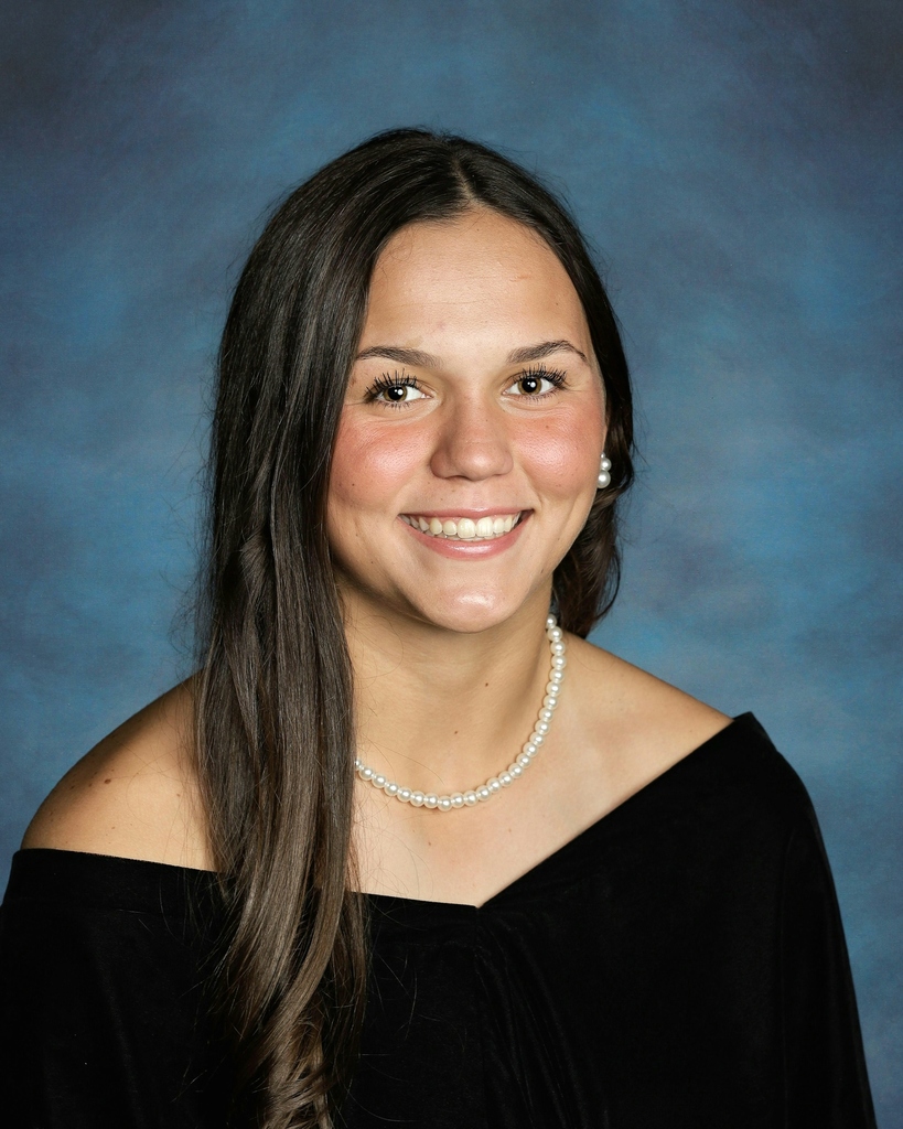 Senior portrait of Kayden wearing a black shirt, white pearl necklace, with a blue background