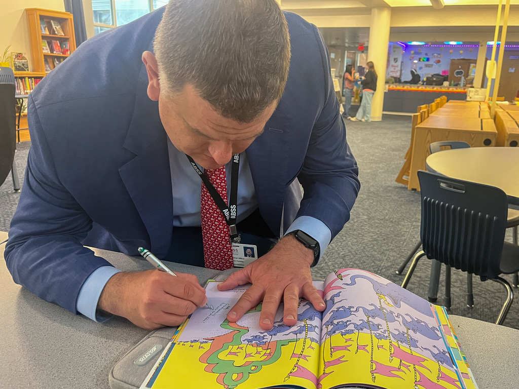 A close-up shot of Dr. Fleming's hands as he uses a silver pen to sign a personalized note inside a graduation-themed children's book for a student.