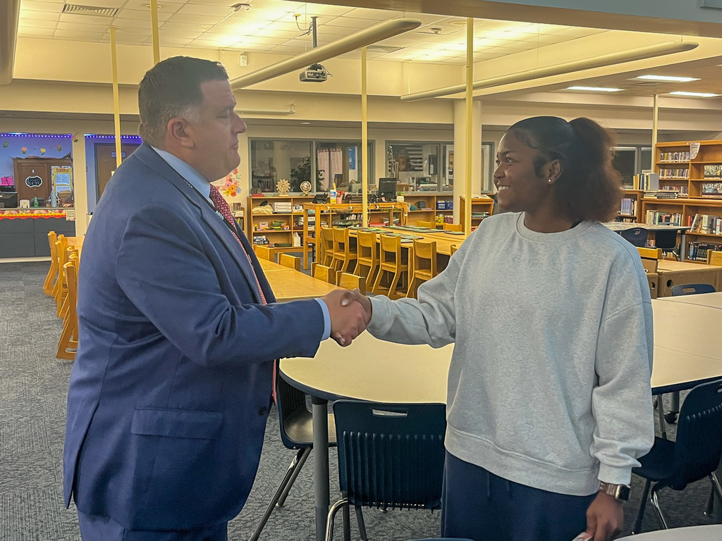 Superintendent Dr. FlemingDr. Fleming smiles while shaking hands with a female student in a gray sweatshirt inside the high school media center.