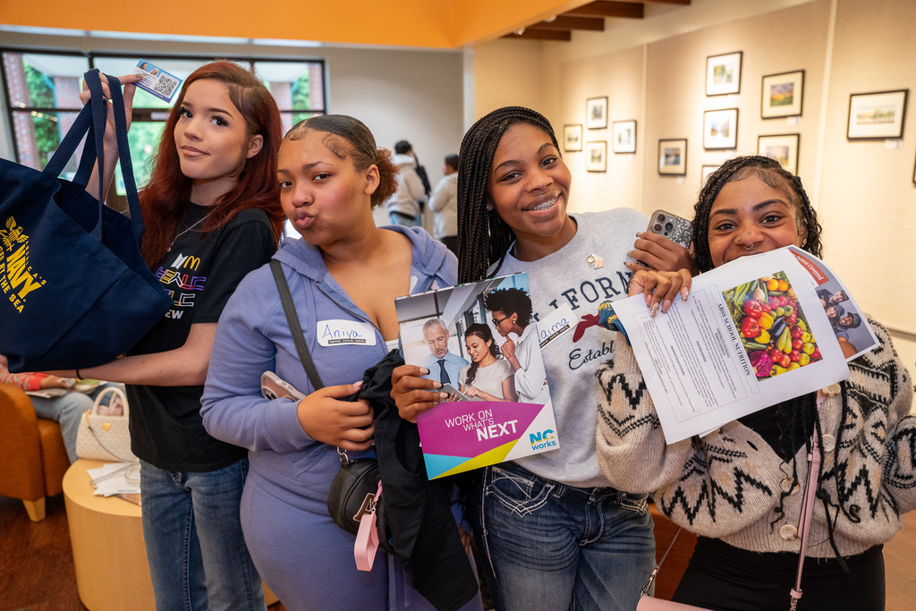 Four female students holding job fair materials in the lobby of the Mebane Arts Center