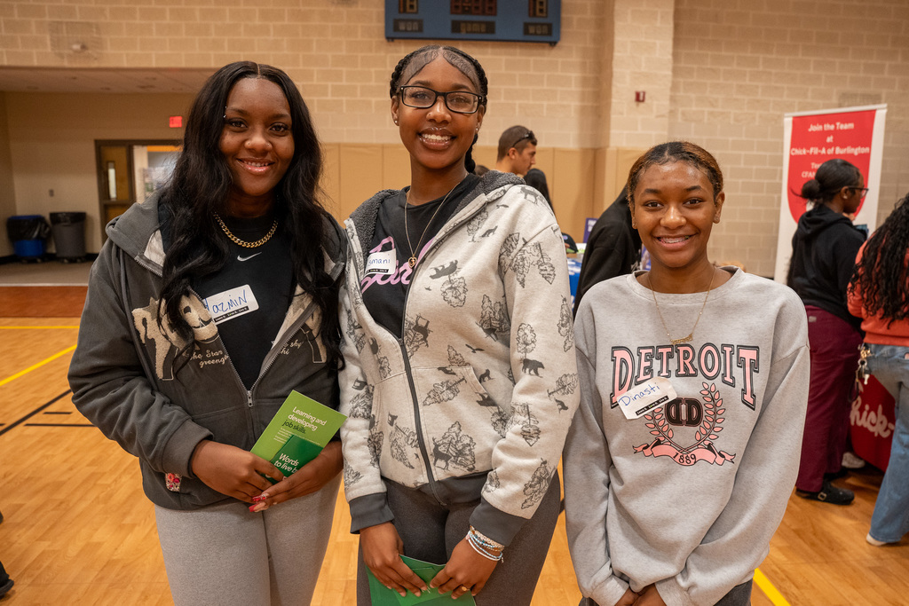 Three females students pose for a photo among other high school students at the Senior Job Fair