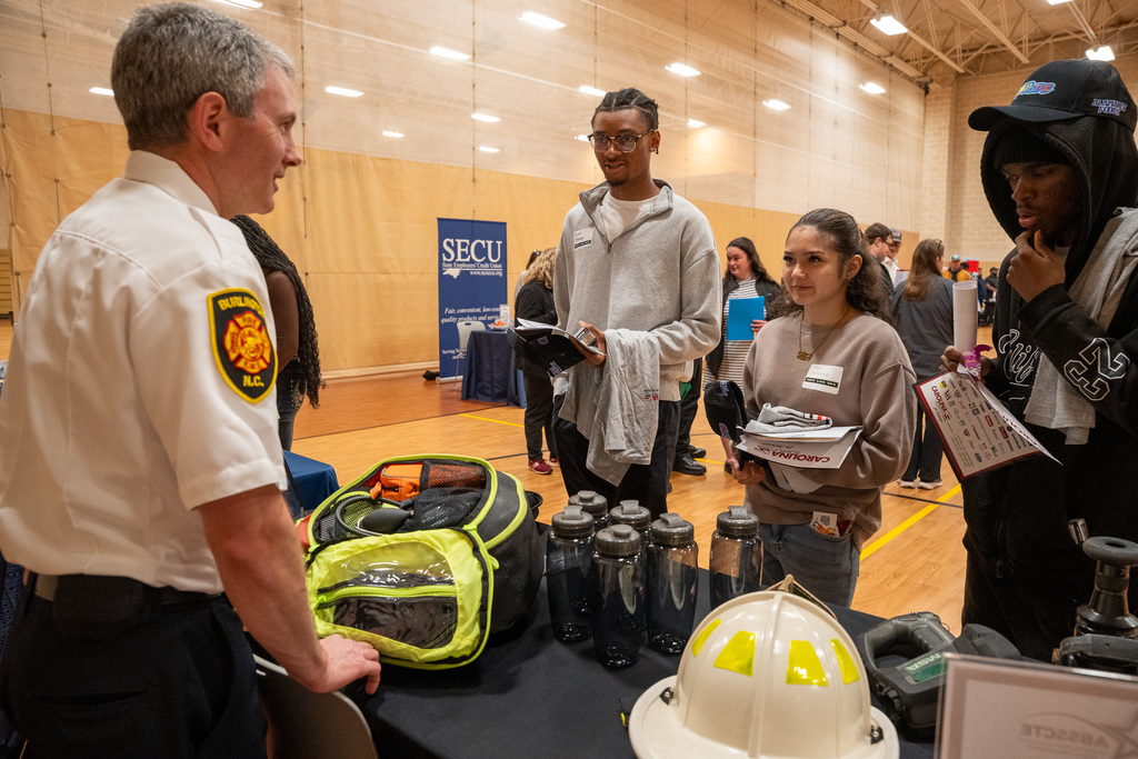Three students talk with a Burlington Fire Department representative at the Job Fair
