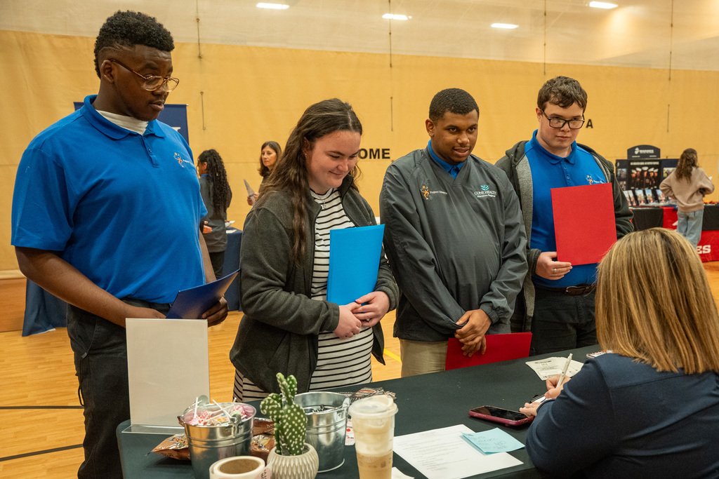 Four students look towards a job application table at the Senior Job Fair