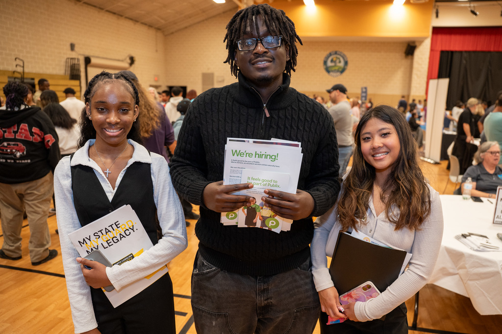 Three students, two girls and one boy, holding job fair materials in the Mebane Arts Center