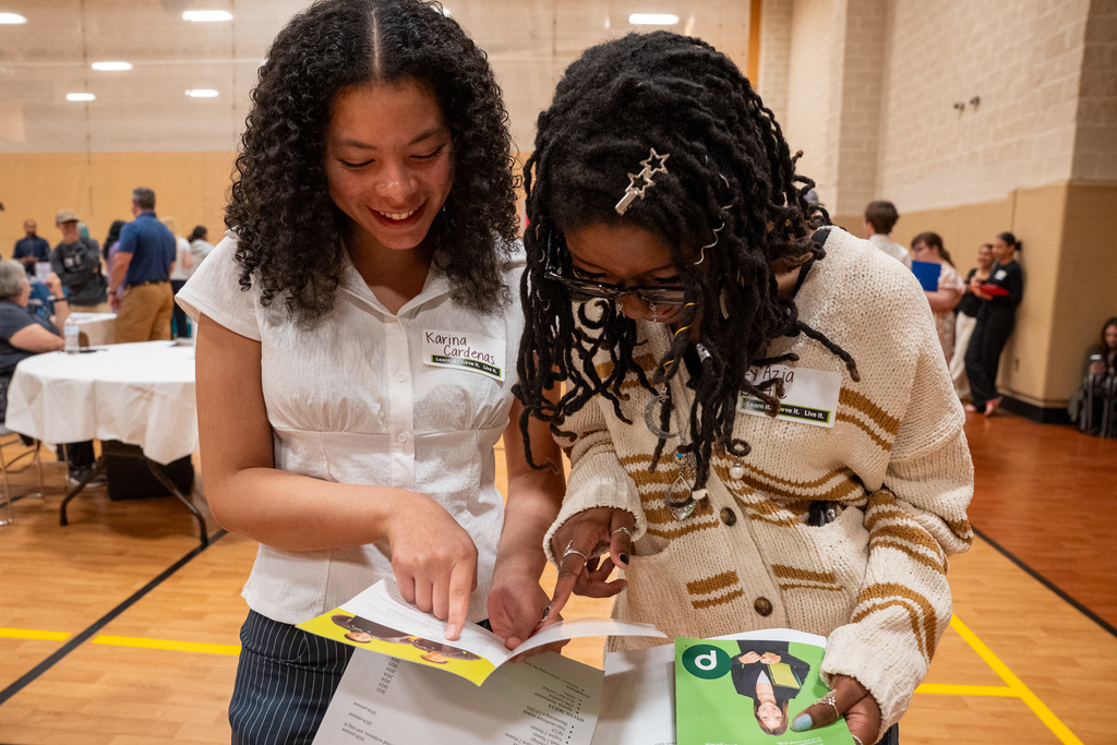 Two girls look closely at a packet of materials at the Job Fair