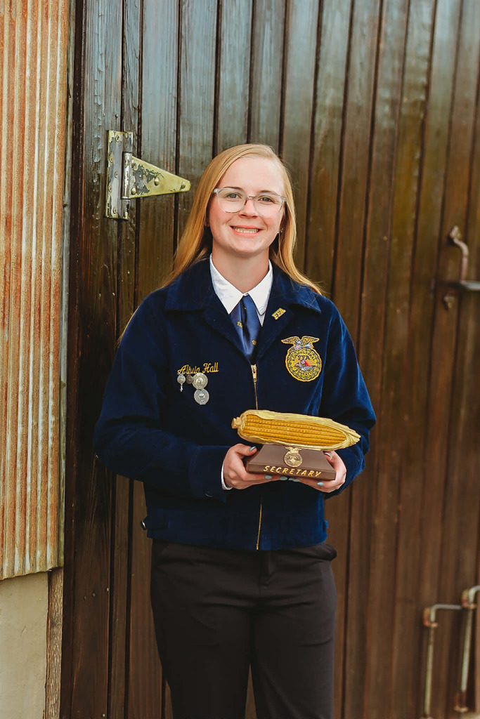 Alivia holding a corn trophy and wearing blue FFA attire