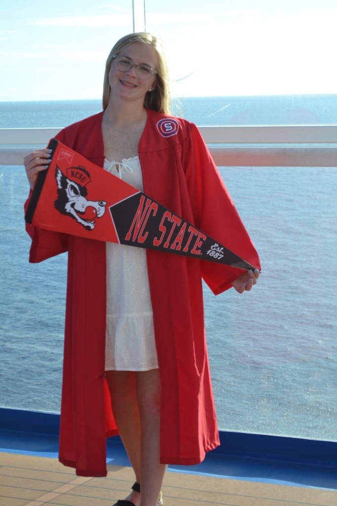Alivia wearing red Southern Alamance graduation robes and holding a NC State banner