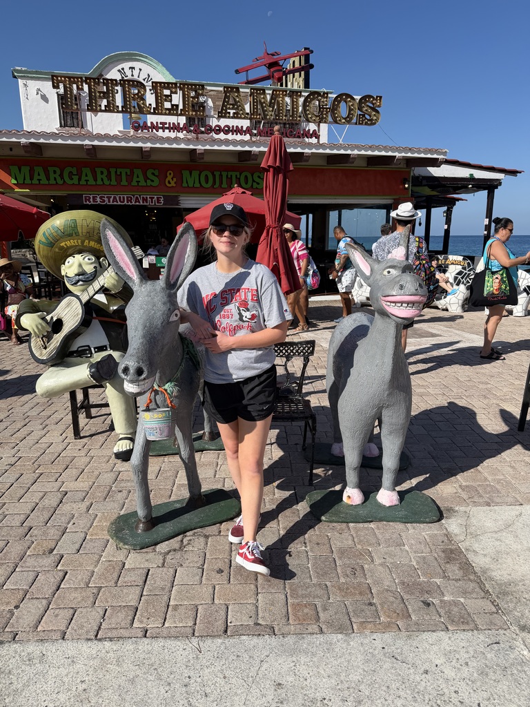 Alivia standing with donkeys in front of a Three Amigos restaurant