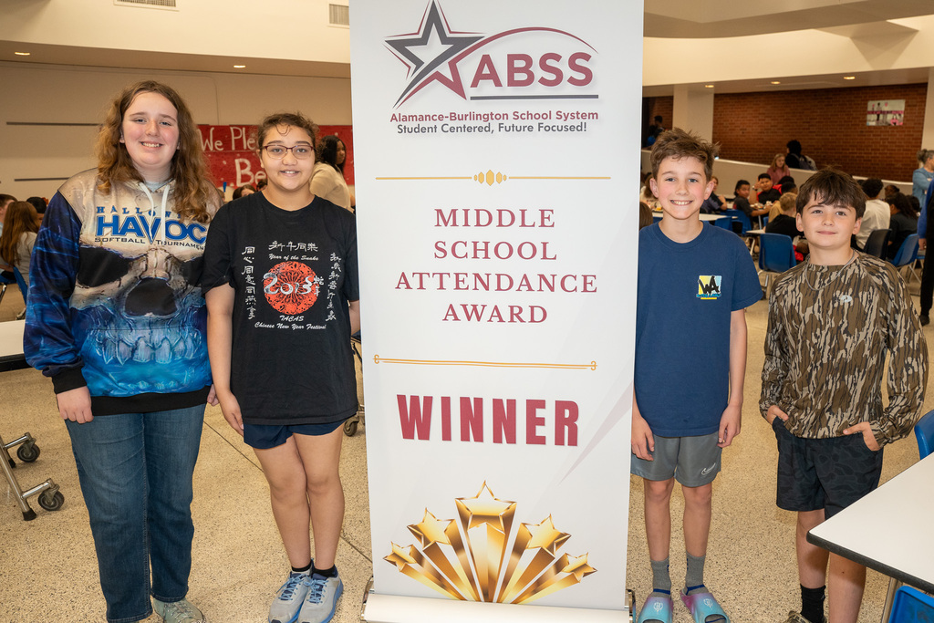 Four middle school students standing next to a Middle School Attendance Award Winner banner in the school cafeteria