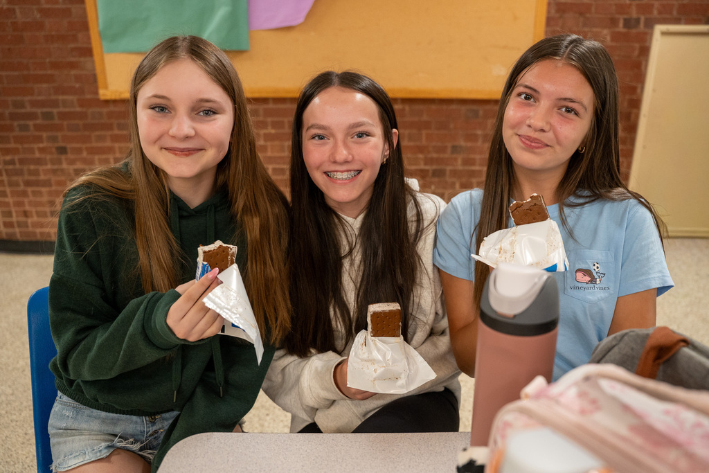 Three middle school girls hold their free ice cream up with big smiles on their faces