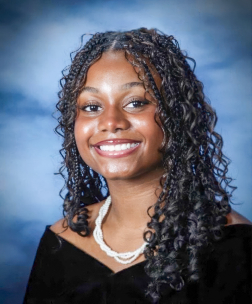 School portrait of Chloe wearing a formal black shirt, white necklace, with a blue backdrop