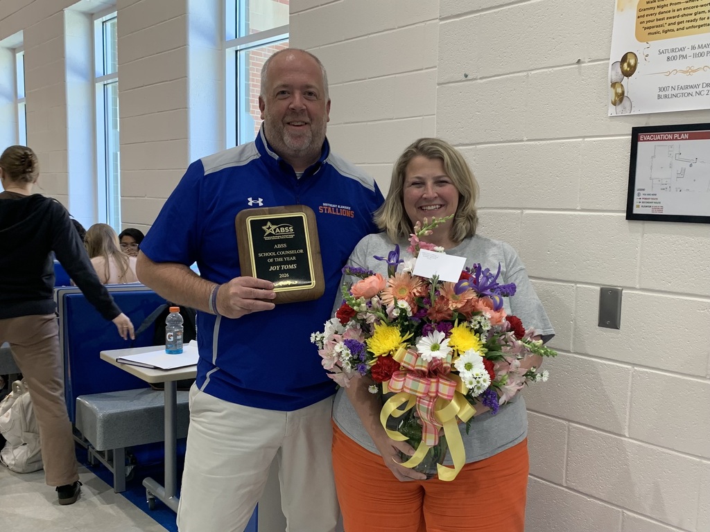 Joy Toms holding a large flower arrangement beside Principal Yarborough who is holding her recognition plaque