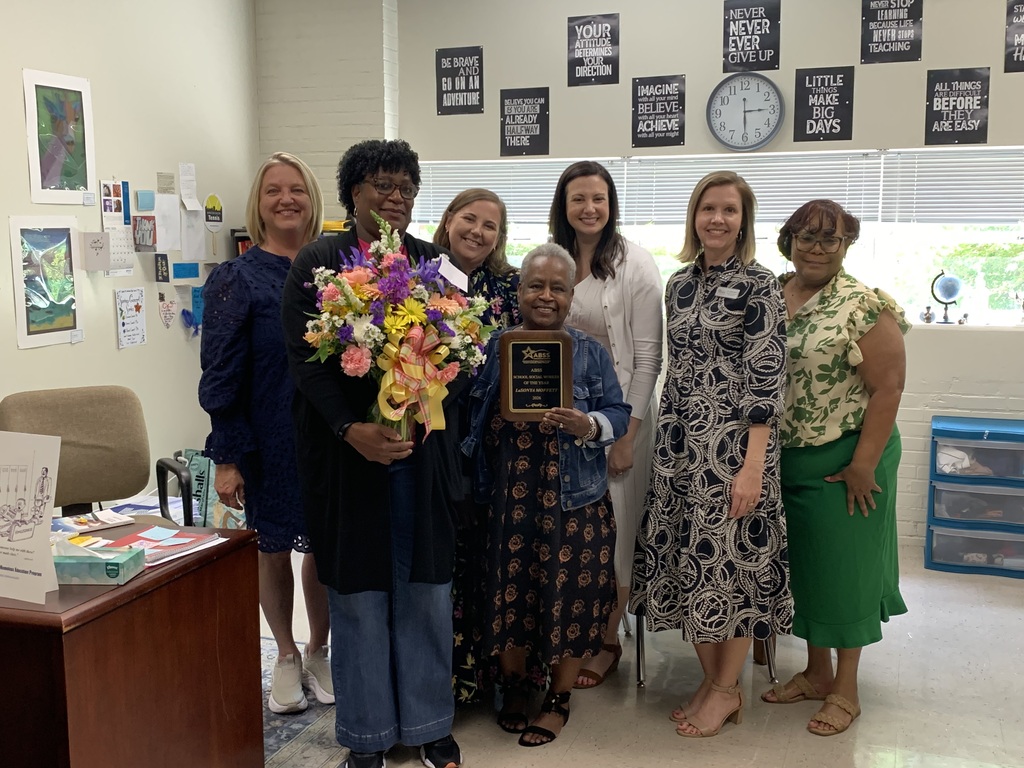 LaSonya standing in her office with Student & Family Services staff holding a flower bouquet and holding an award plaque