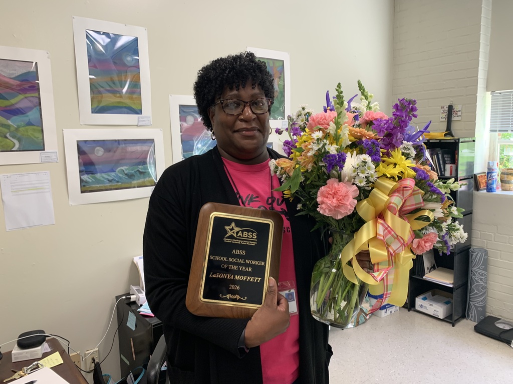 LaSonya standing in her office holding a flower bouquet and holding an award plaque