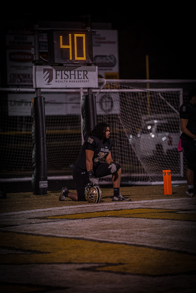 Kinston in black Bulldogs football gear kneeling on the field