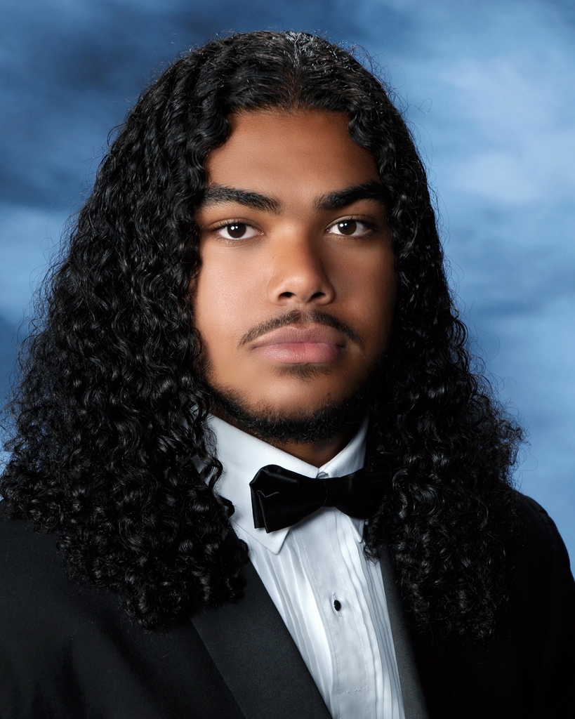 Kinston in a formal senior portrait wearing tuxedo against a blue background