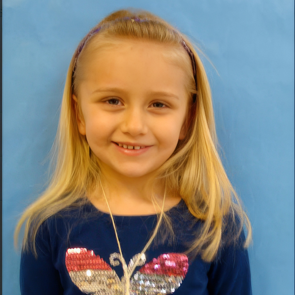 A young girl wearing a sequined butterfly shirt smiles for a school photo
