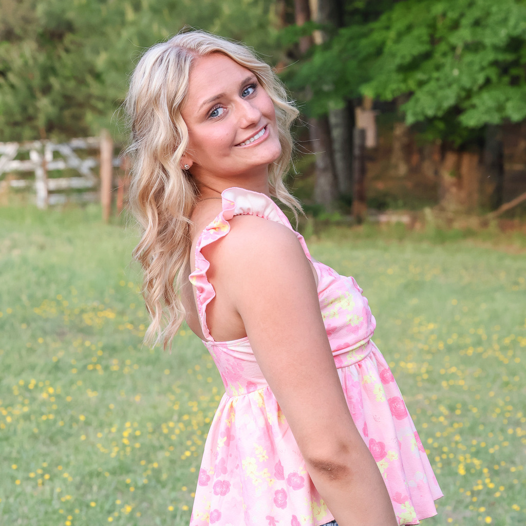 A high school senior wearing a pink dress provides an over the shoulder posed smile